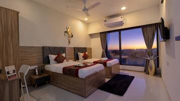 Una habitación de hotel moderna con dos camas, un escritorio, una silla, un ventilador de techo, un equipo de aire acondicionado y un ventanal con vistas a la ciudad.