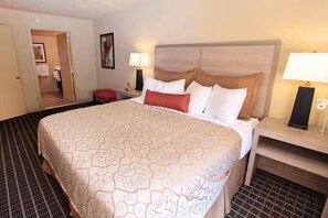 A hotel room with a large bed, two bedside tables with lamps, a red chair, and a door leading to another room. - Vacation Village Resort at Patriots Inn (Richmond Rd Williamsburg)