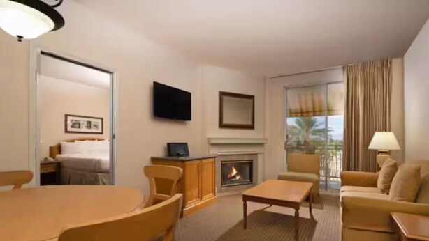 A hotel room with a dining table, chairs, a sofa, a TV, a fireplace, and a large window with curtains. - Club De Soleil: Usher & Chris Brown R&B Suite! (Las Vegas)