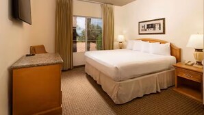 A hotel room with a bed, a desk, a chair, a TV, a window with curtains, and a picture on the wall. - Club De Soleil: Usher & Chris Brown R&B Suite! (Las Vegas)