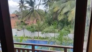 A balcony with wooden railings and chairs, overlooking a swimming pool and palm trees. - Oga Reach Yala (thissamaharama)
