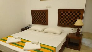 A neatly made bed with a striped bedspread, two pillows, a nightstand with a lamp, and a wall with a checkered pattern. - Oga Reach Yala (thissamaharama)