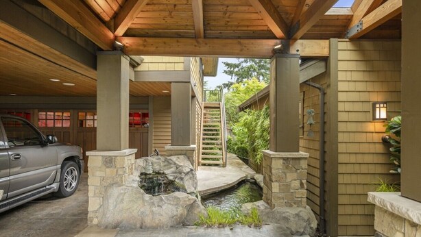 A covered garage with a stone waterfall feature, a wooden staircase, and a vehicle parked inside.