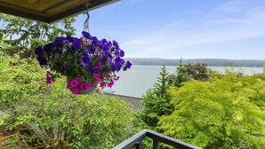 A hanging flower basket with purple flowers, a wooden ceiling, and a view of a lake with trees in the background.