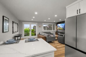 Eine moderne Küche mit einem großen Kühlschrank, ein Essbereich mit Tisch und Stühlen sowie ein Wohnbereich mit Sofa und Fernseher.