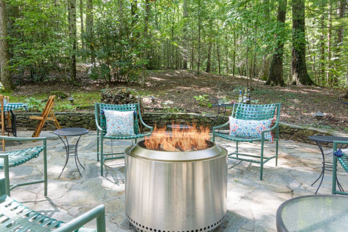 An outdoor patio with a fire pit, stone flooring, and green chairs with patterned cushions.