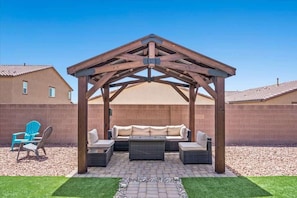 Ein überdachter Patio-Bereich mit einer Holz-Pergola, Gartenmöbeln und einer Ziegelwand.