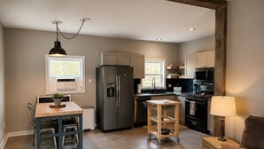 A modern kitchen with a refrigerator, stove, and microwave. There is a dining table with chairs and a small stool. - This house is a 2 bedroom(s), 2 bathrooms, located in Kalkaska, MI. (Kalkaska)