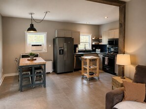 A modern kitchen with a refrigerator, stove, and microwave. There is a dining table with chairs and a small stool.