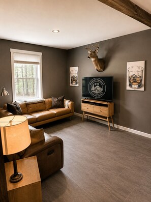 A living room with a leather sofa, a mounted deer head, a television, and framed artwork.