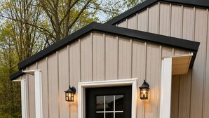 A building with a black door, white trim, and two wall-mounted lanterns. - This house is a 2 bedroom(s), 2 bathrooms, located in Kalkaska, MI. (Kalkaska)