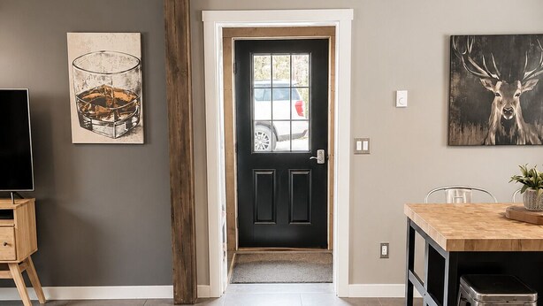 A modern kitchen with a wooden beam ceiling, a black door, and a dining area with a bar stool. - This house is a 2 bedroom(s), 2 bathrooms, located in Kalkaska, MI. (Kalkaska)