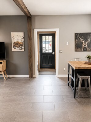 A modern kitchen with a wooden beam ceiling, a black door, and a dining area with a bar stool.