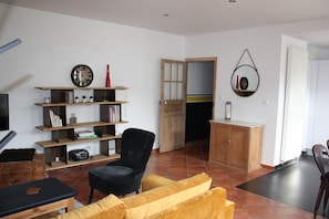 Ein Wohnzimmer mit schwarzem Sessel, gelbem Sofa, Holzregalen, einem Fernseher und einem Holzkabinett.