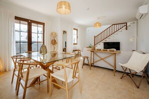 Ein geräumiger Wohnbereich mit einem Glastisch, Holzsesseln, einer Couch, einem Fernseher und einer Treppe.