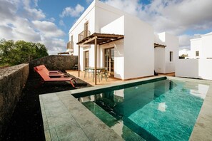 Une maison moderne dotée d’une piscine, d’un espace salon extérieur et d’un mur en pierre.