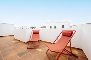 Eine Dachterrasse mit zwei roten Liegestühlen und einem gefliesten Boden.