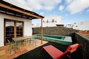 Une terrasse avec une table et des chaises, une petite piscine et un mur en pierre.