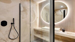 A modern bathroom with a glass-enclosed shower, a round mirror with built-in lighting, and a marble-tiled wall. - AN AUTHENTIC PARISIAN LIVING AT BLVD SAINT GERMAIN (Paris)