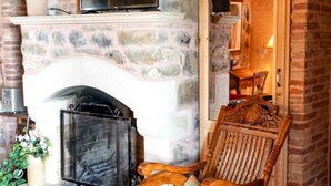 A stone fireplace with a television above it, a rocking chair in front, and a brick wall. - Vacation home  by Interhome (Anatoli)