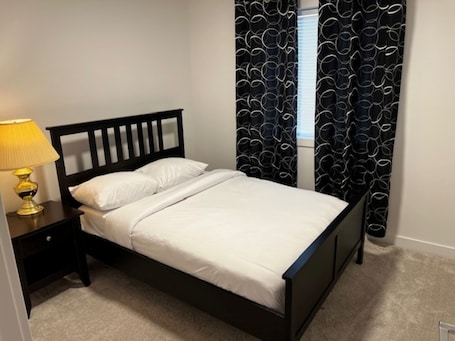 A single bed with a wooden headboard, a bedside table with a lamp, and black patterned curtains.. Lakeview Oasis
