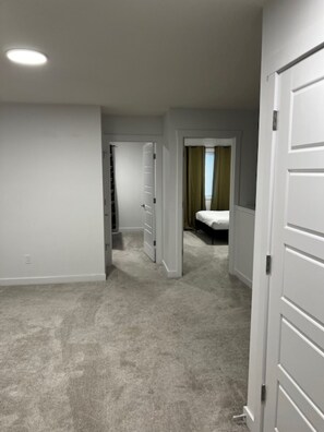 A hallway with carpeted floors, white walls, and a bed with a green curtain in the background. - Lakeview Oasis (Edmonton)