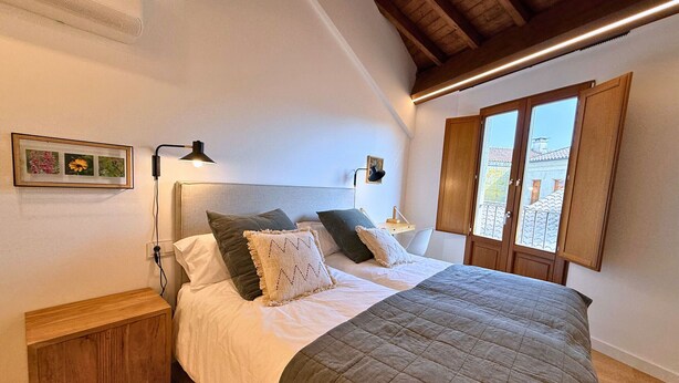 Een slaapkamer met een bed, nachtkastjes, een wandlamp, een ingelijst schilderij en een raam met uitzicht.