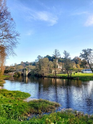 Ein Fluss mit einer Steinbrücke, grünen Ufern und Bäumen.