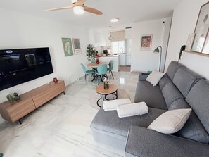 Ein modernes Wohnzimmer mit Flachbildfernseher, einer Couch, einem Esstisch mit Stühlen und einer Küche im Hintergrund.
