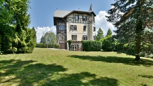 Une maison à deux étages, de conception traditionnelle, avec une pelouse bien entretenue et un grand arbre sur le côté droit.