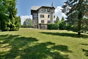 A two-story house with a traditional design, a well-maintained lawn, and a large tree to the right. - Villa Plemelj - Apartment Plemelj - sleeps 2 guests  in 1 bedroom (Bled)