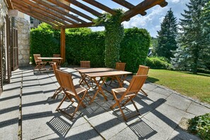 An outdoor patio with a pergola, wooden tables and chairs, stone flooring, and a hedge in the background. - Villa Plemelj - Apartment Plemelj - sleeps 2 guests  in 1 bedroom (Bled)