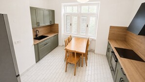 Une cuisine moderne avec une table à manger, des meubles de couleur claire et une fenêtre équipée de stores.