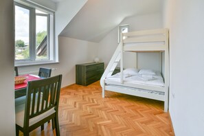 Ein Zimmer mit einem Etagenbett, einem Esstisch mit Stühlen, einem Fenster und einem Fischgrätparkettboden.