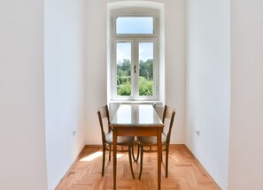 Ein Essbereich mit Tisch und Stühlen, ein Fenster mit Blick auf Grünflächen und eine weiße Wand.