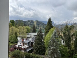 Et hus med skråt tag, balkon og udsigt over en sø og skovklædte bakker.