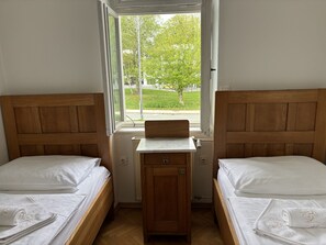 Et værelse med to træsenge, et lille skrivebord og et vindue med udsigt til grøn vegetation.