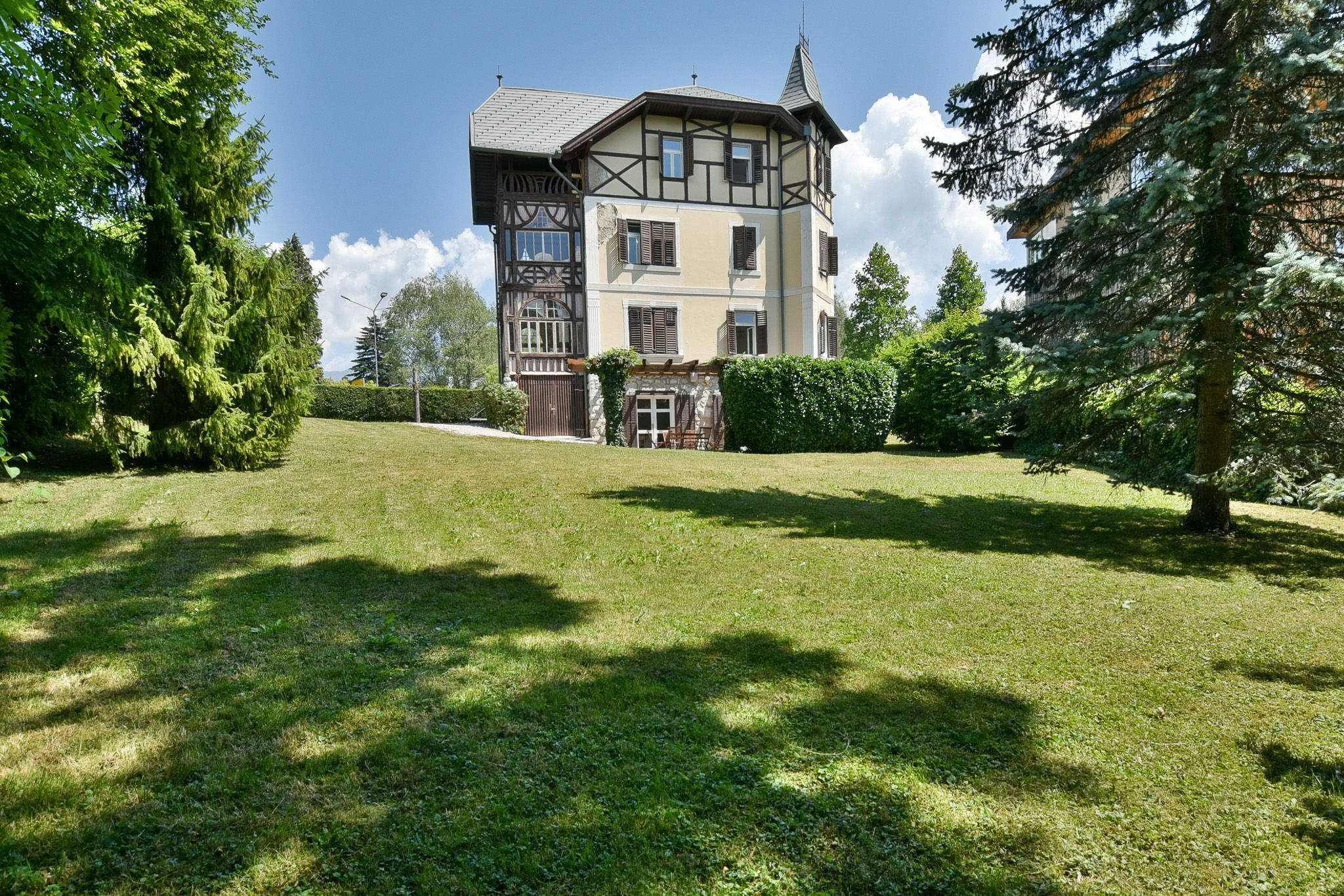 Ein zweistöckiges Haus im traditionellen Stil, ein gepflegter Rasen und ein großer Baum zur Rechten.