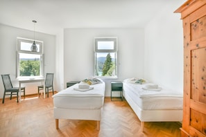 A room with two beds, a desk, and two chairs. There are windows with views of trees and mountains. - Villa Plemelj - Apartment Stefan - sleeps 2 guests  in 1 bedroom (Bled)