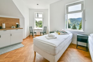 Ein Schlafzimmer mit Bett, Schreibtisch, Stuhl, einem Fenster mit Blick und einer Küchenzeile.