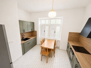 Eine moderne Küche mit Esstisch, hellen Schränken und einem Fenster mit Jalousien.