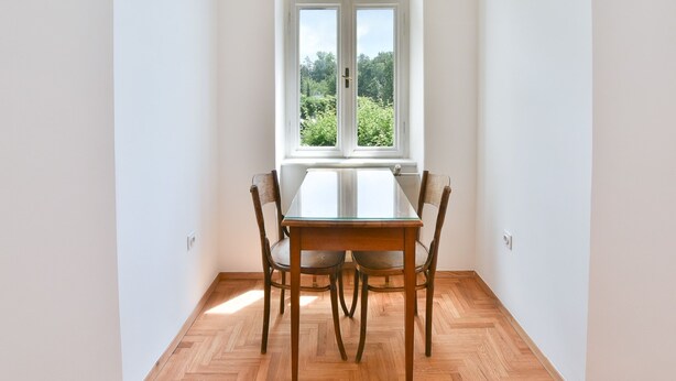 Un comedor con una mesa y sillas, una ventana con vista a zonas verdes y una pared blanca.