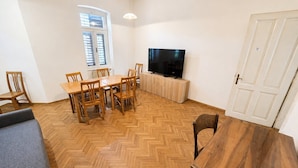 A room with a herringbone wooden floor, a dining table with chairs, a television on a cabinet, and a door. - Villa Plemelj - All 4 Apartments - sleeps 8 guests  in 4 bedrooms (Bled)