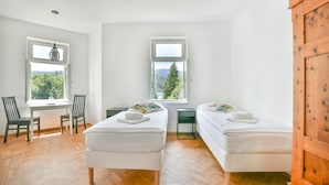 A room with two beds, a desk, and two chairs. There are windows with views of trees and mountains. - Villa Plemelj - All 4 Apartments - sleeps 8 guests  in 4 bedrooms (Bled)