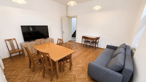 A living room with a wooden herringbone floor, a grey sofa, a wooden dining table with chairs, a flat-screen TV, and pendant lights. - Villa Plemelj - All 4 Apartments - sleeps 8 guests  in 4 bedrooms (Bled)