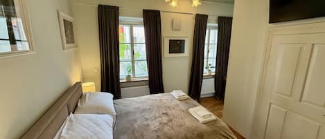 Une chambre à coucher avec un lit, un lustre, une fenêtre avec des rideaux, une porte et un radiateur.