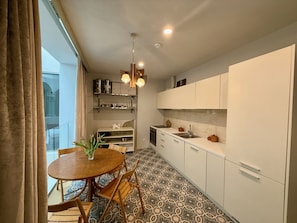 A modern kitchen with white cabinets, a round wooden table, and patterned floor tiles.