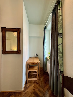 Un pasillo estrecho con una mesa y una silla de madera, un radiador y una ventana con cortinas.