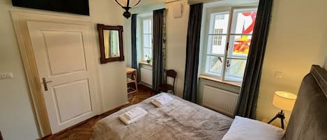 Une chambre à coucher avec un grand lit, un plancher en bois, une fenêtre avec des rideaux, un bureau et une chaise.