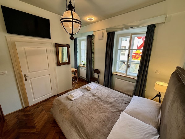 Un dormitorio con una cama grande, suelo de madera, una ventana con cortinas, un escritorio y una silla.